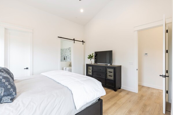 A bedroom with a bed, a TV, a dresser, and a door.