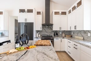 A modern kitchen with white cabinets, a stainless steel refrigerator, a gas stove, and a marble countertop.