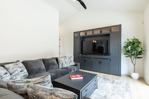 A modern living room with a grey sofa, a black coffee table, a flat-screen TV, and a potted plant.