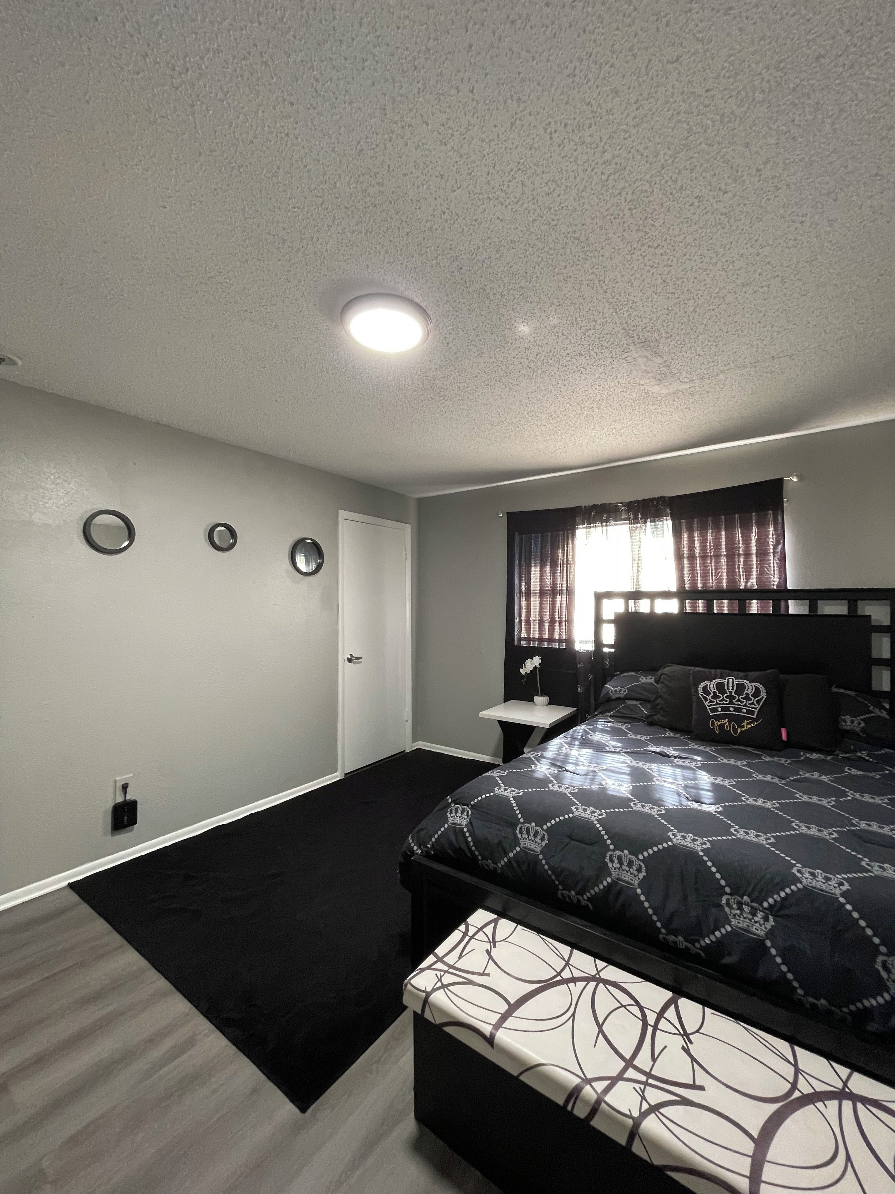 Quarto com cama, mesa de cabeceira, janela com cortinas e luminária na parede.