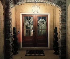 A double door entrance with a welcome mat, two wreaths, and a hanging light fixture. - Lakefront Auburn Game Day Retreat (Auburn)