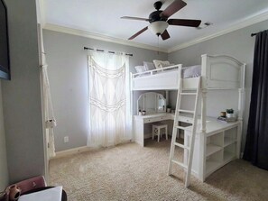 Una habitación con literas, un escritorio, una silla, un ventilador de techo y una ventana con cortinas.