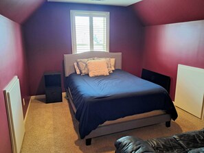 Un dormitorio con cama, ventana, radiador y una mesita de noche.