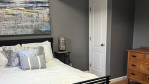 Une chambre à coucher avec un lit, une table de chevet, une commode et un tableau au mur.