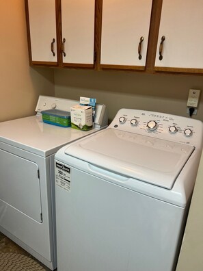 Une buanderie équipée d’un lave-linge et d’un sèche-linge à chargement frontal, d’un meuble en bois au-dessus et d’une prise de courant sur le mur.