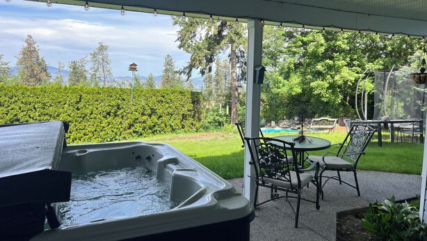 Un bain à remous situé sous un patio couvert, avec vue sur un jardin et une piscine.