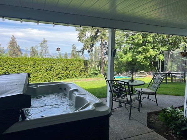 Boblebad under et overdækket terrasseområde med udsigt til en have og en swimmingpool.
