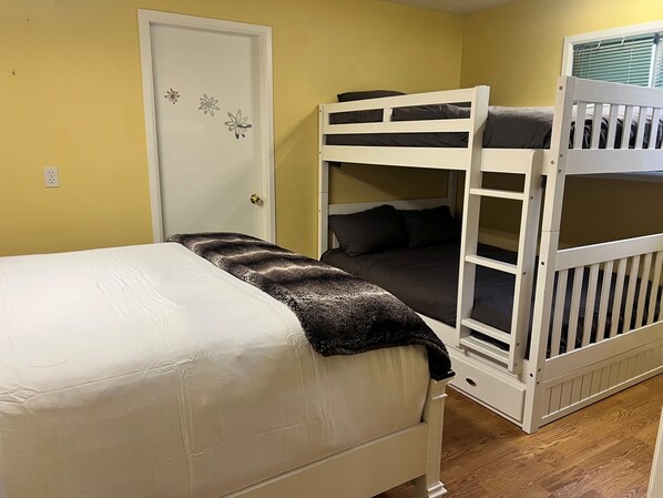 Un lit superposé avec une structure blanche et un lit simple avec un matelas blanc et une couverture foncée.