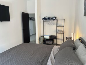 Ein Schlafzimmer mit einem Bett, einem Kleiderschrank, einem Regal mit gefalteter Kleidung und einem an der Wand befestigten Fernseher.
