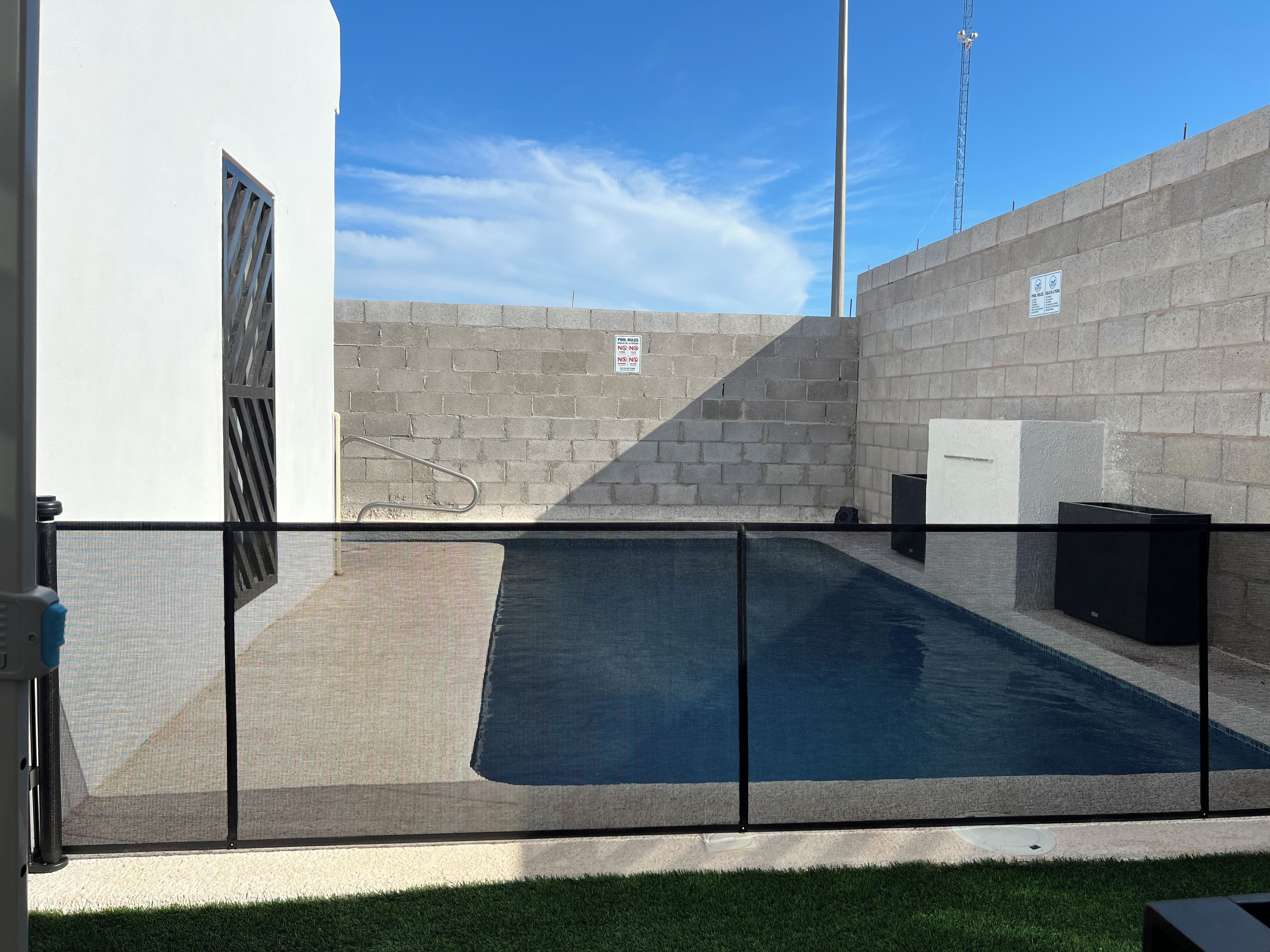 A pool area with a metal fence, a concrete wall, and a clear sky.