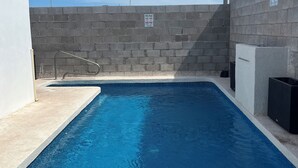 Una piscina rectangular con superficie de agua azul cristalina, rodeada por una plataforma de concreto y un muro bajo.