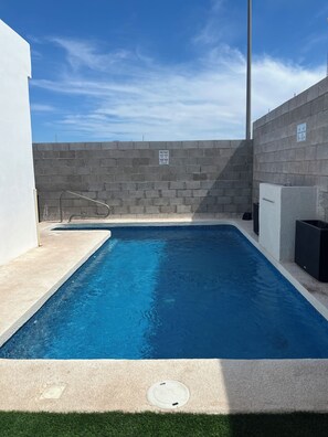 Ein rechteckiger Swimmingpool mit einer klaren blauen Wasseroberfläche, umgeben von einer Betonplattform und einer niedrigen Mauer.