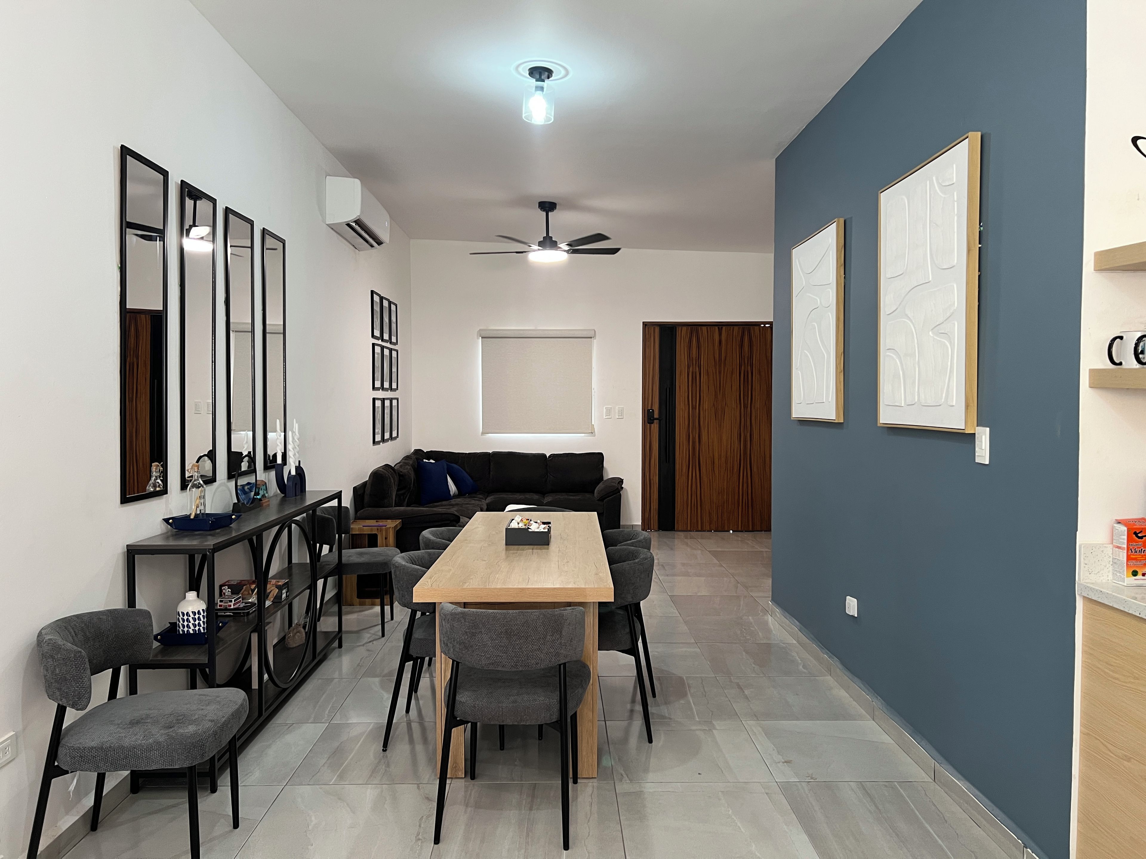 A modern living room with a sofa, dining table, chairs, and a ceiling fan.