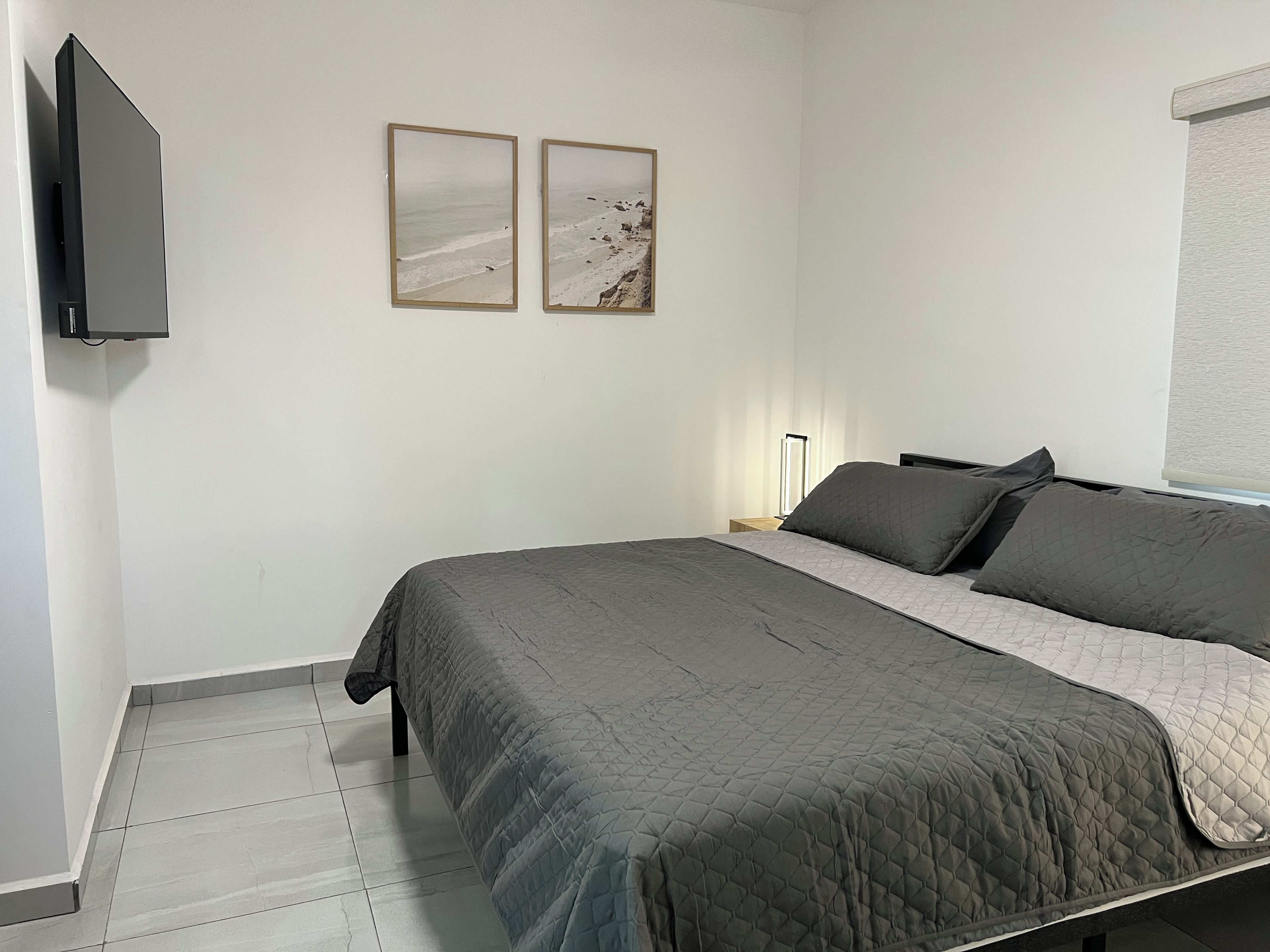 A bedroom with a bed, a nightstand, a lamp, and two framed pictures on the wall.