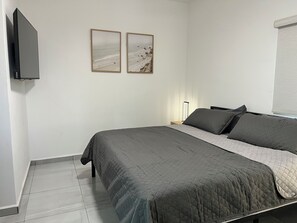 Un dormitorio con una cama, una mesita de noche, una lámpara y dos cuadros en la pared.
