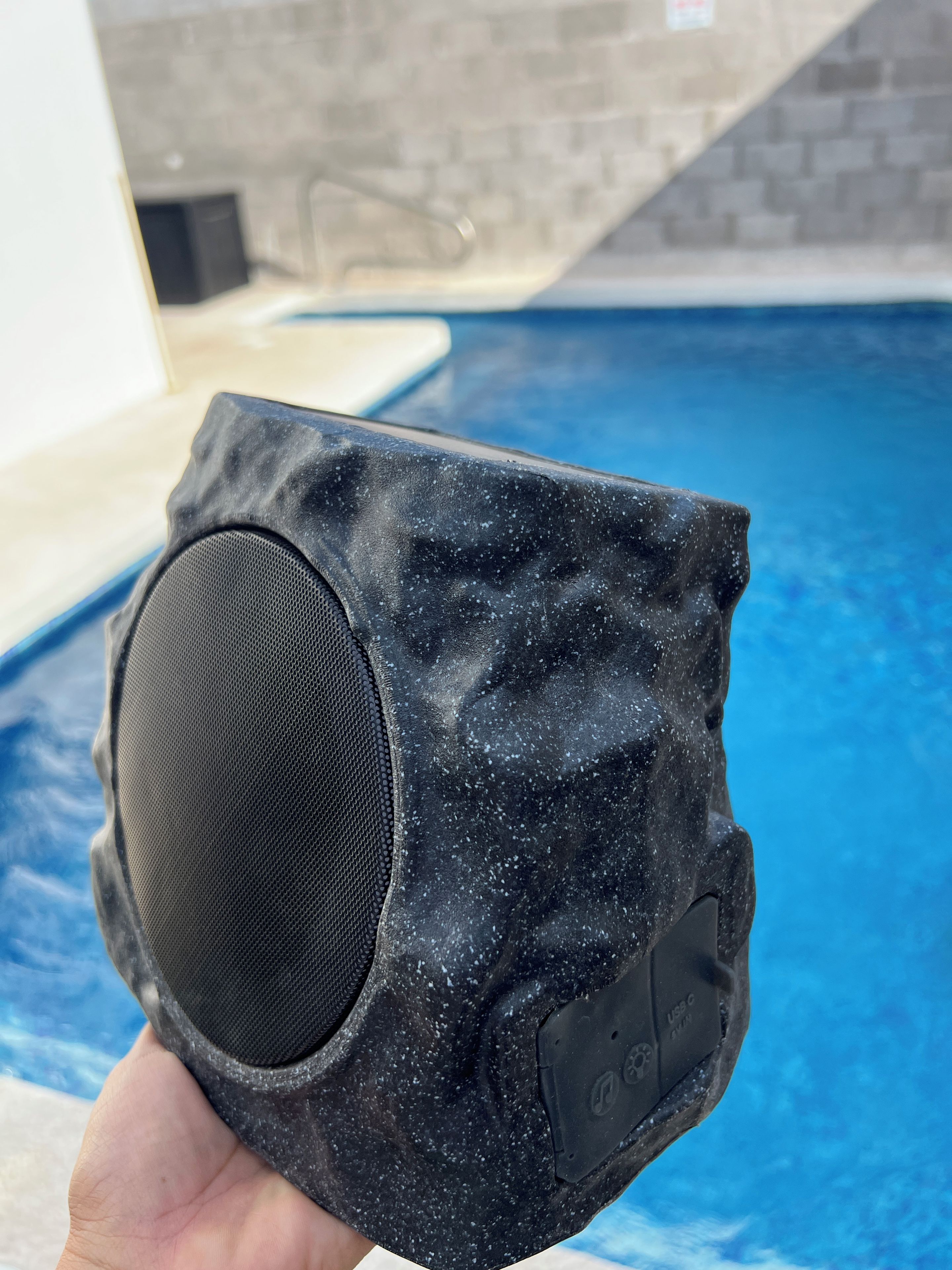 A black object with a textured surface, held in a hand, with a pool and tiled walls in the background.