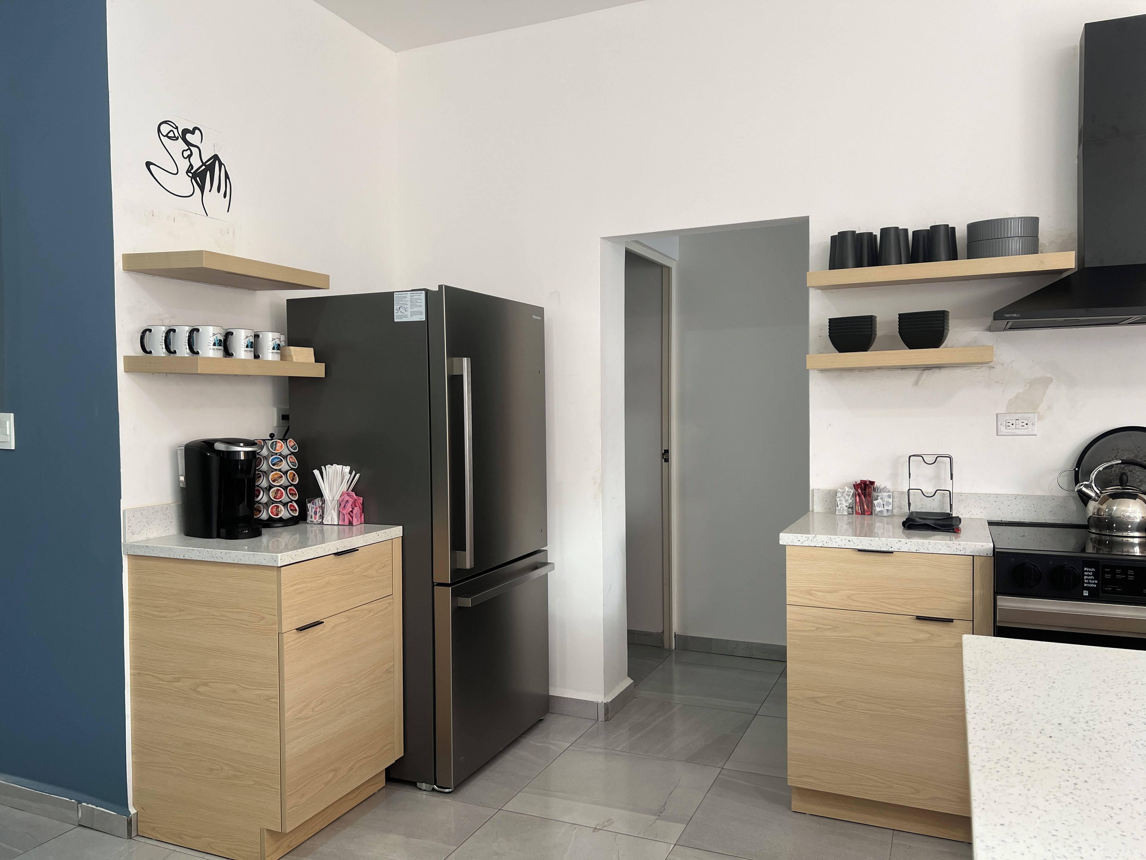 A modern kitchen with a stainless steel refrigerator, wooden cabinets, and a countertop with a coffee maker and utensils.