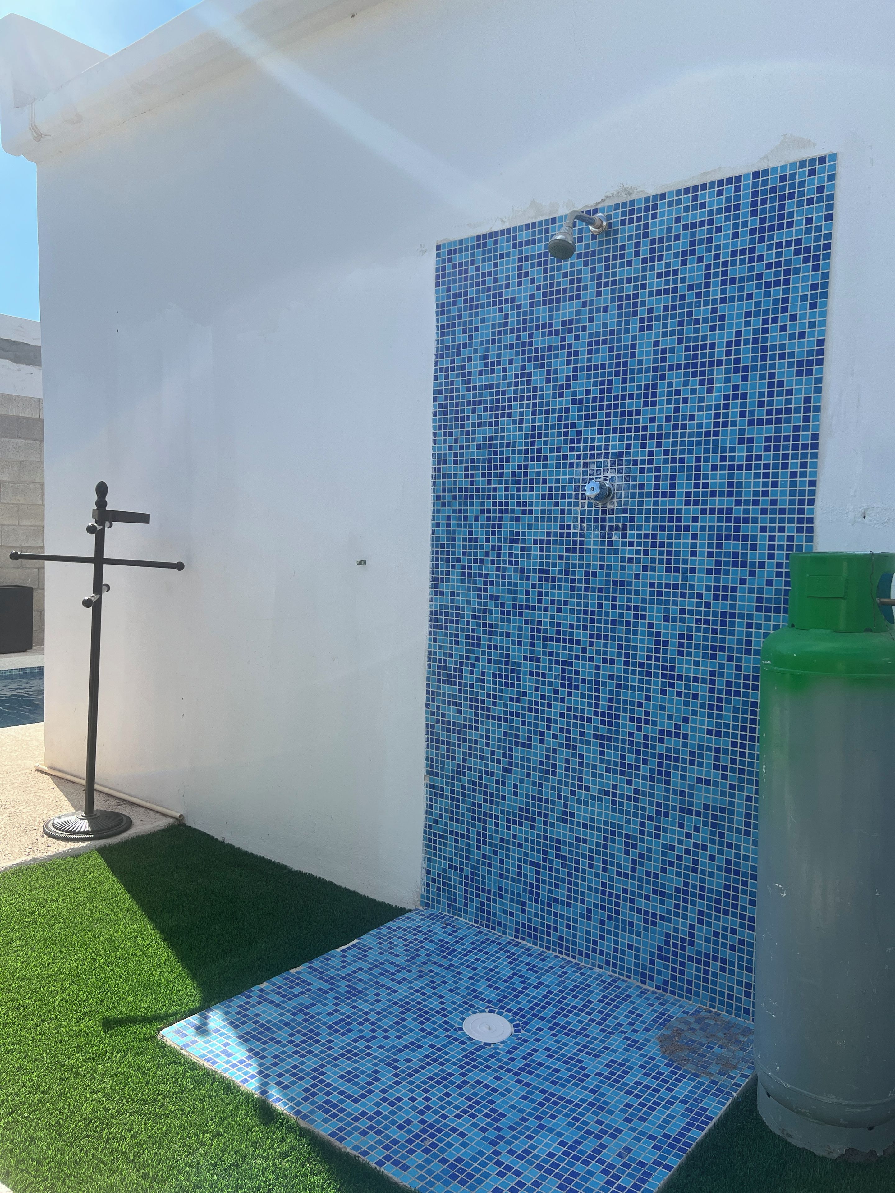 A small outdoor area with a tiled wall, a metal stand, and a green container.