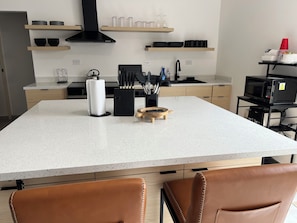 A modern kitchen with a large island, wooden cabinets, and a black microwave on a cart.