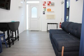 A room with a dark sofa, a small table with a chair, a white door, and emergency exit signs on the wall.