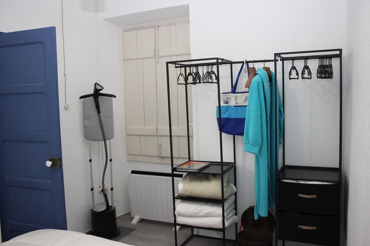 Ein Zimmer mit einer blauen Tür, einem schwarzen Metallschrank zur Aufbewahrung von Kleidung, einem Heizkörper und einem kleinen Tisch mit einem Buch.
