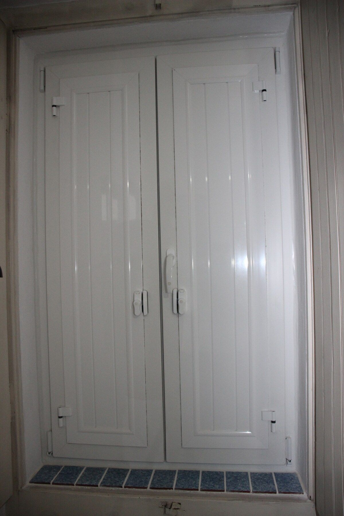 Puerta doble blanca con pomo y una pequeña ventana en la parte inferior.