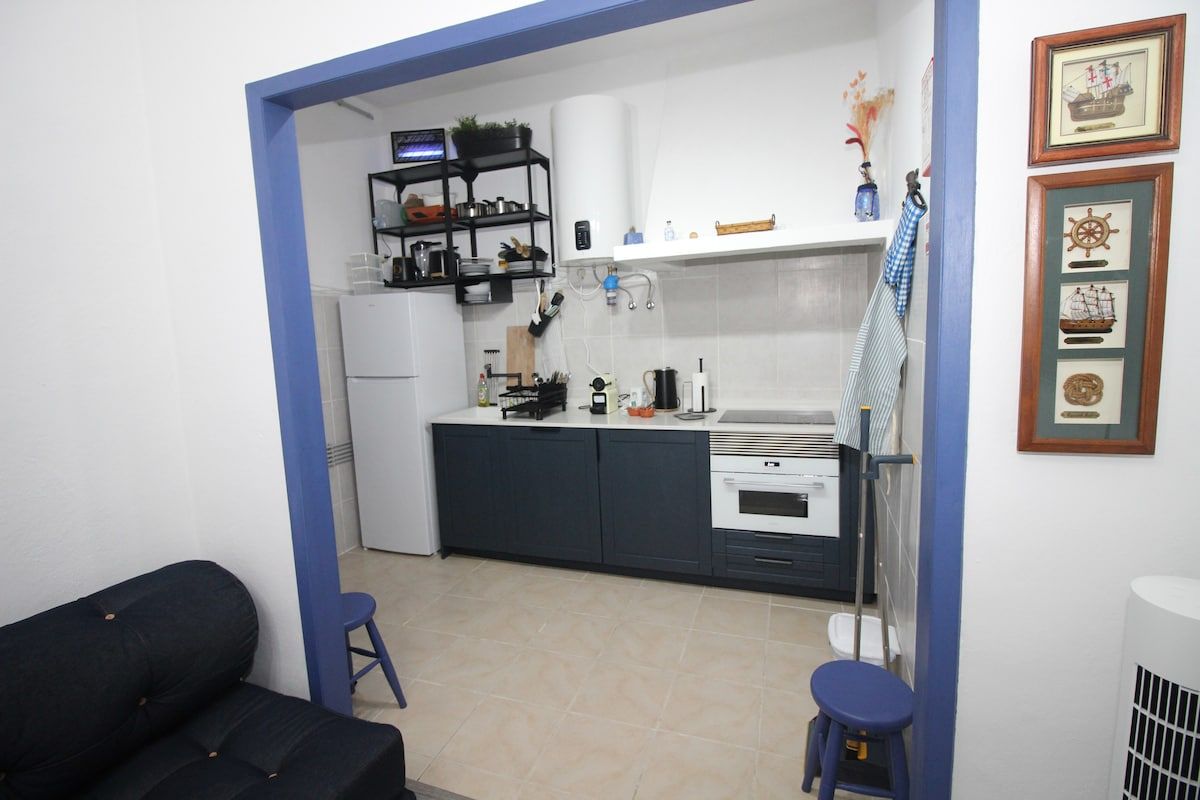 A compact kitchen with dark cabinets, a white countertop, and a small dining area with stools.