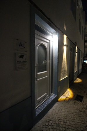 Un carreró estret amb una porta il·luminada per una cinta de llum. Un rètol sobre la porta diu 'AL' i un altre cartell a sota indica 'LOCAL VIGIADO'.