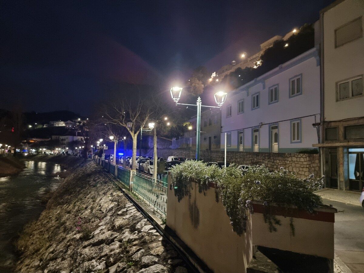 A nighttime street scene with a stone pathway, street lamps, and buildings with balconies.