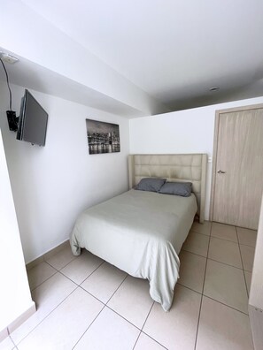 Ein Schlafzimmer mit einem Bett, einem an der Wand befestigten Fernseher und einer Tür.