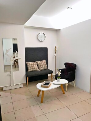 Ein modernes Wohnzimmer mit einer Couch, einem Sessel, einem Couchtisch, einer Wanduhr und einem Ziertepiegel.