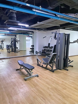 Ein Fitnessraum mit Trainingsgeräten, einer Bank und einem Hantelständer.