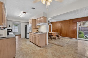 A spacious kitchen with wooden cabinets, a dining area with a table and chairs, and a view of a backyard through a sliding glass door. - 3BR Near White Rock Lake - Fire Pit & BBQ Grill (Dallas)