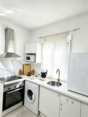 Cuina moderna amb forn integrat, microones i rentadora, un obrador d'acer inoxidable i una finestra amb persianes.