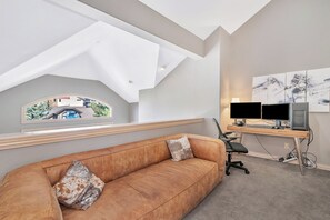 A modern room with a sloped ceiling, a large window with a view, a desk with two monitors, a leather sofa, and a painting on the wall. - Ironwood 16 - 4 Bedroom Ski In Ski Out Next to the Gondolas + EZCancel (Steamboat Springs)