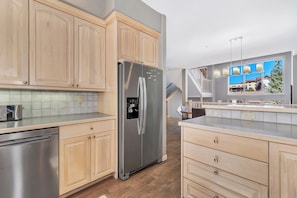 A modern kitchen with wooden cabinets, stainless steel appliances, and a view of a residential area. - Ironwood 16 - 4 Bedroom Ski In Ski Out Next to the Gondolas + EZCancel (Steamboat Springs)