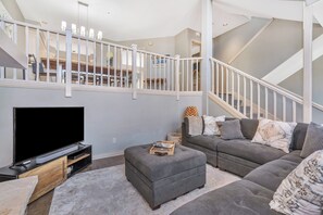 A modern living room with a flat-screen TV, grey sofas, a wooden coffee table, and a staircase. - Ironwood 16 - 4 Bedroom Ski In Ski Out Next to the Gondolas + EZCancel (Steamboat Springs)