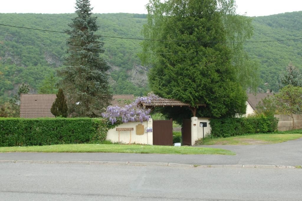 Une entrée fermée par un portail, avec un petit bâtiment, le tout entouré de verdure et de collines.