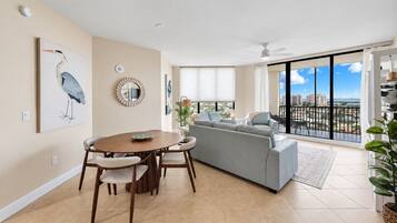 Un vaste espace de vie comprenant une table à manger, un canapé gris et un balcon offrant une vue sur la ville.