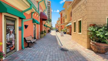 A paved walkway flanked by buildings with colorful facades, a bench, and potted plants.