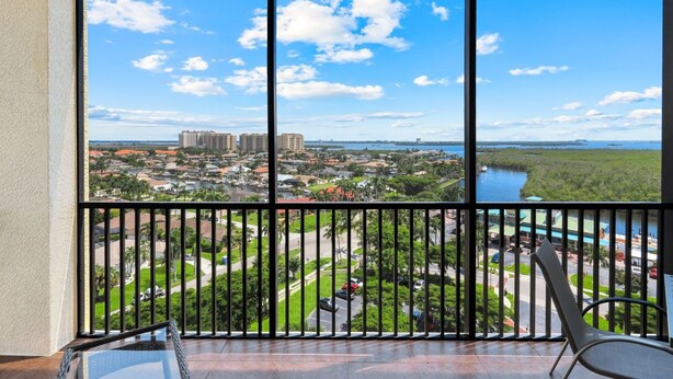 A balcony with a view of a residential area, a body of water, and distant buildings.