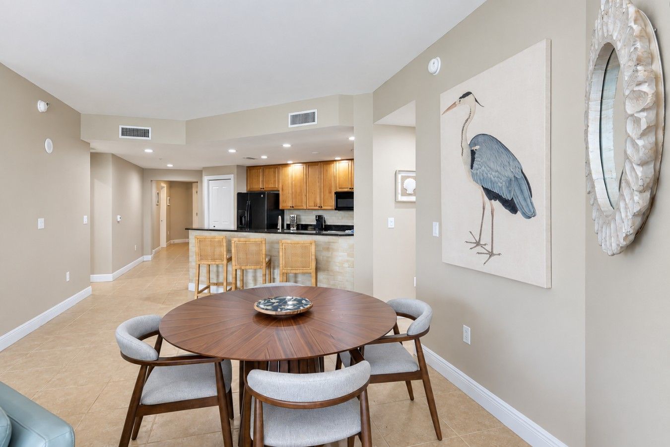 A dining area with a round table, four chairs, and a wall-mounted artwork of a bird.