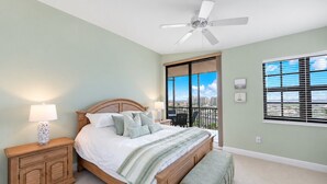 A bedroom with a bed, nightstand, lamp, and a view of the city through large windows.