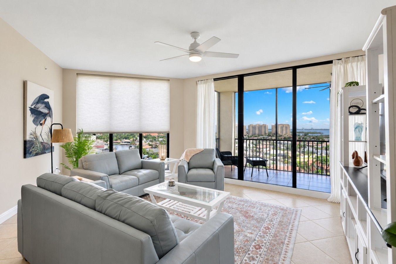 A spacious living room with a balcony, a ceiling fan, and a large window offering a city view.