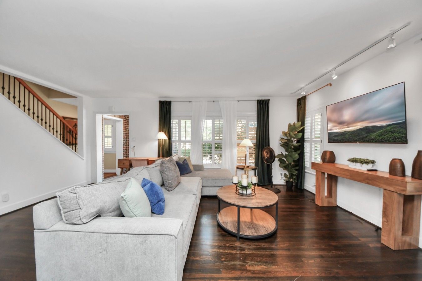 A modern living room with a grey sofa, a round wooden coffee table, and a large flat-screen TV mounted on the wall.
