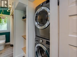 A laundry room with two stacked front-loading washing machines, a white toilet, and a green wall.