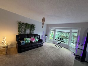 A living room with a black leather sofa, a glass coffee table, a small side table, a keyboard, and a plant. - Bright & Spotless 3BR plus Free parking Perfect for Families & Long Stays (Calgary)