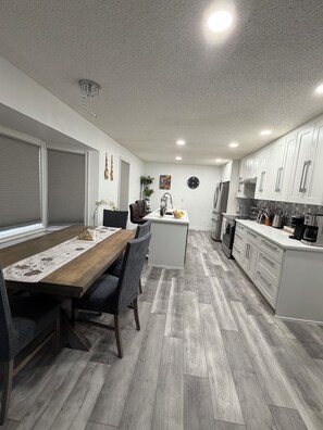 A modern kitchen with white cabinets, a wooden dining table, and a gray herringbone floor. - Bright & Spotless 3BR plus Free parking Perfect for Families & Long Stays (Calgary)