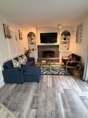 A living room with a sofa, a coffee table, a fireplace, and a flat-screen TV mounted above it. - Bright & Spotless 3BR plus Free parking Perfect for Families & Long Stays (Calgary)