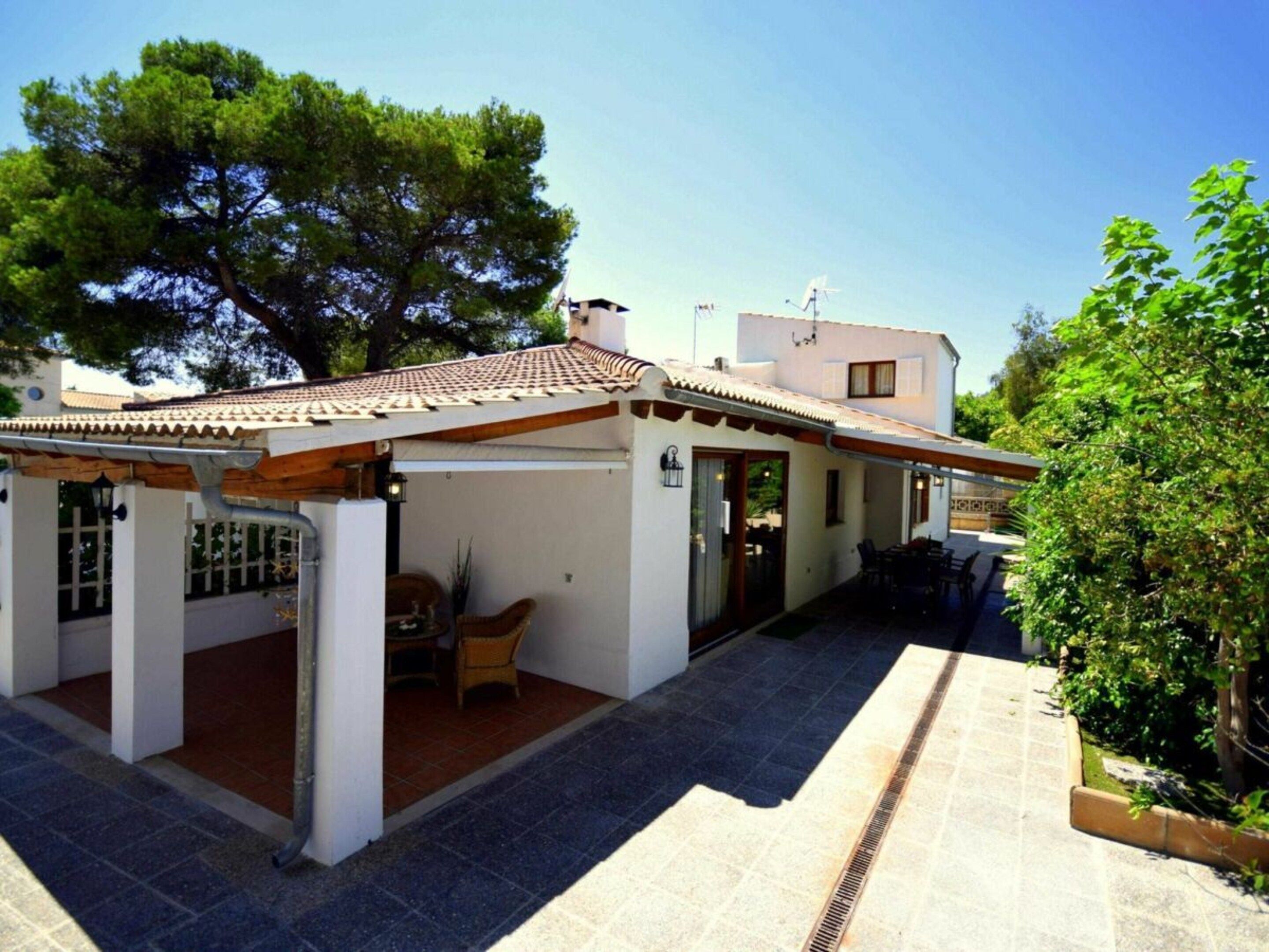 A two-story building with a tiled roof, a covered patio area, and a small garden.